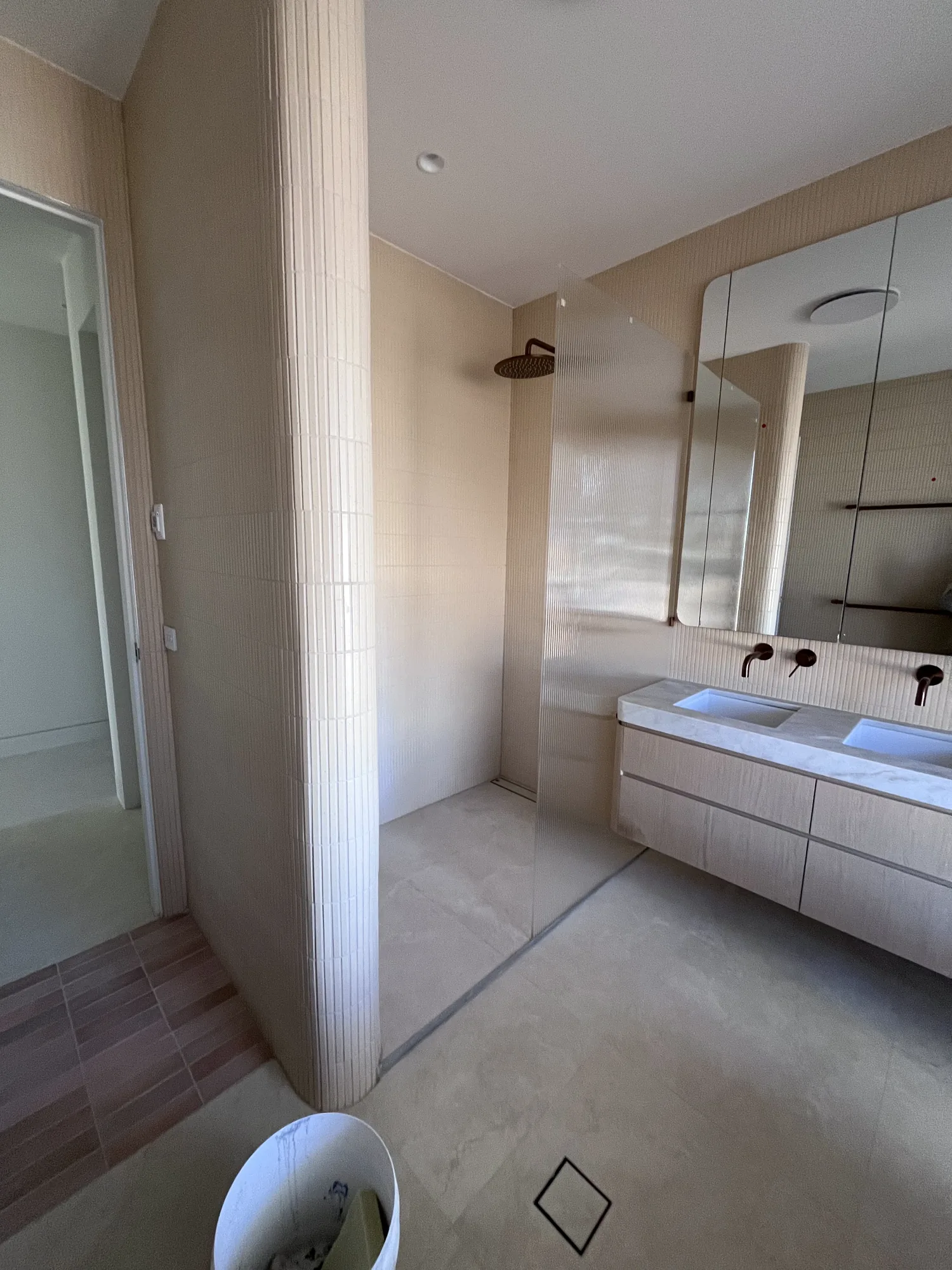 Curved tiled bathroom column, walk-in shower and twin vanity in a residential project.