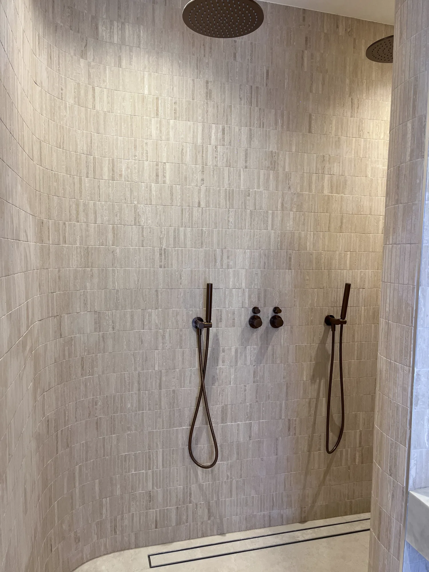 Full-height textured shower tiles with carefully aligned twin fittings and a linear drain.